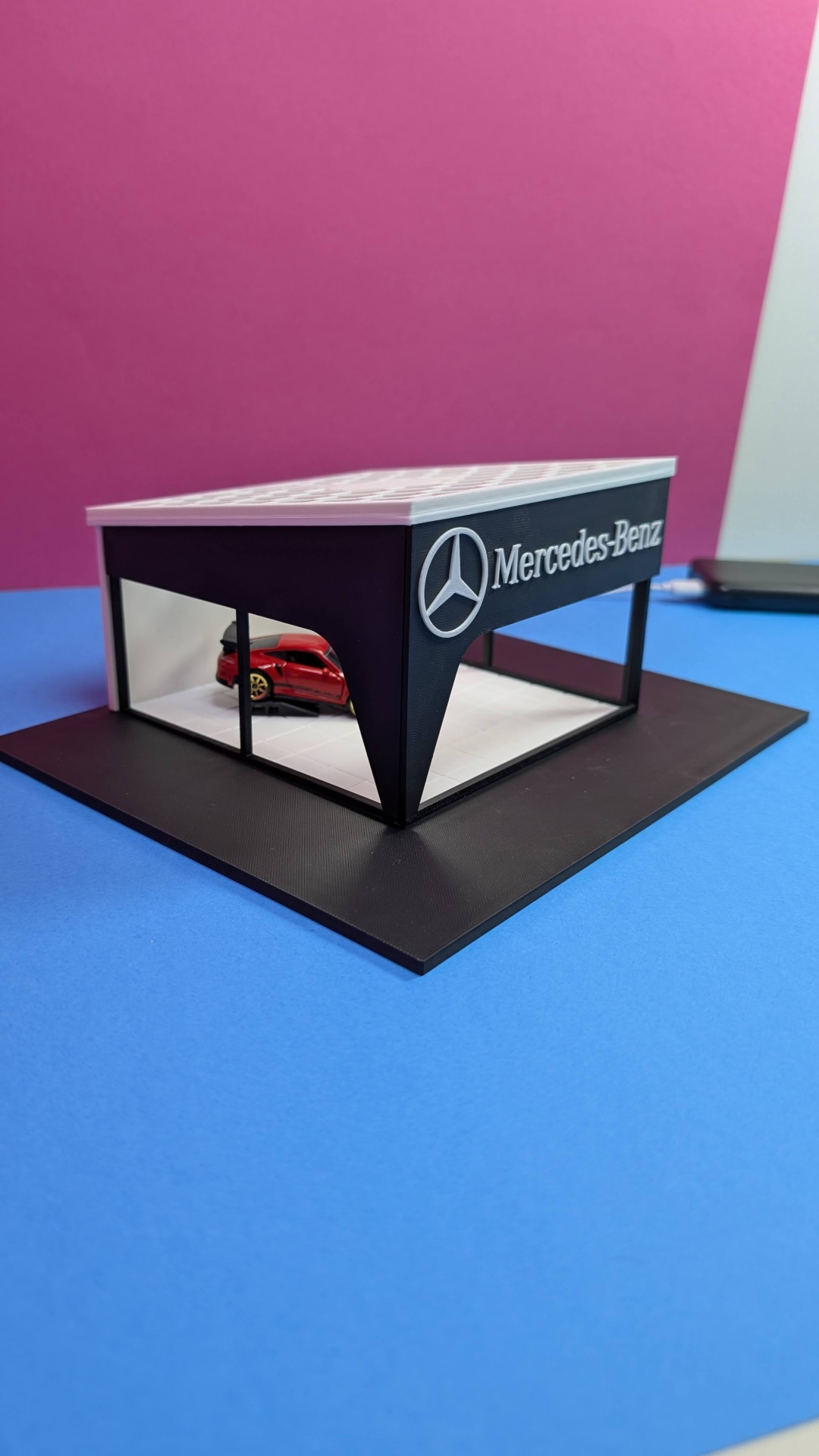 Maquete de concessionária Mercedes-Benz com carro vermelho, fundo rosa e superfície azul