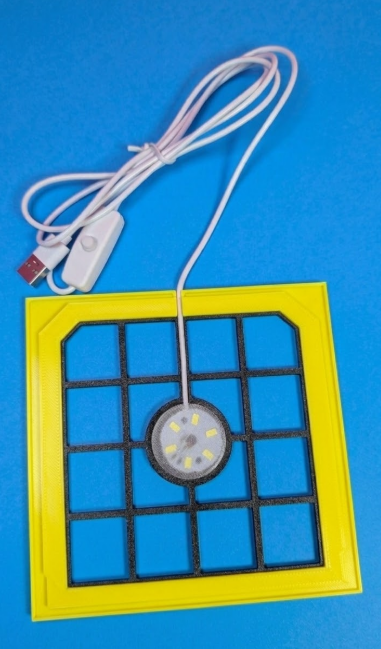 Mesa quadrada amarela com grelha preta e luz LED, cabo USB branco, fundo azul