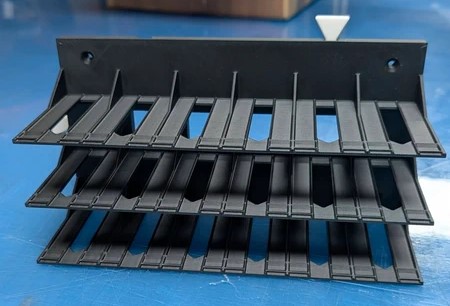 Suporte preto de plástico com três camadas e ranhuras verticais sobre superfície azul