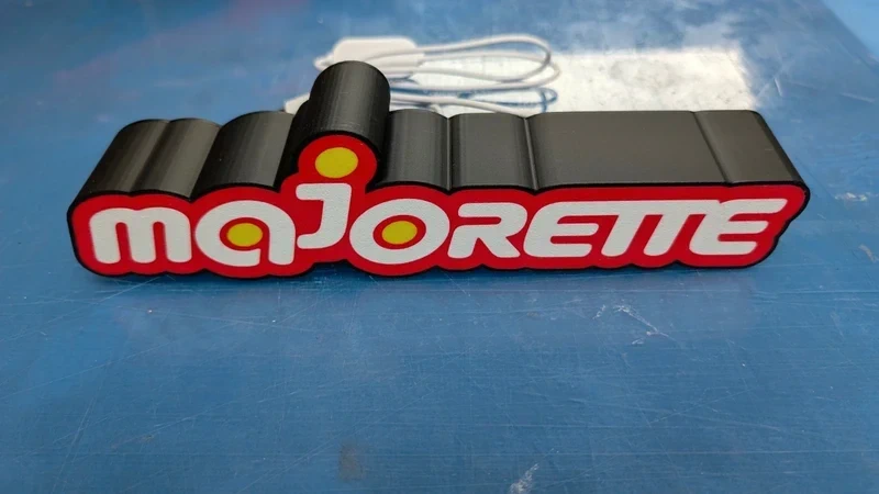 Letreiro decorativo com a palavra majorette em letras brancas e vermelhas sobre fundo preto