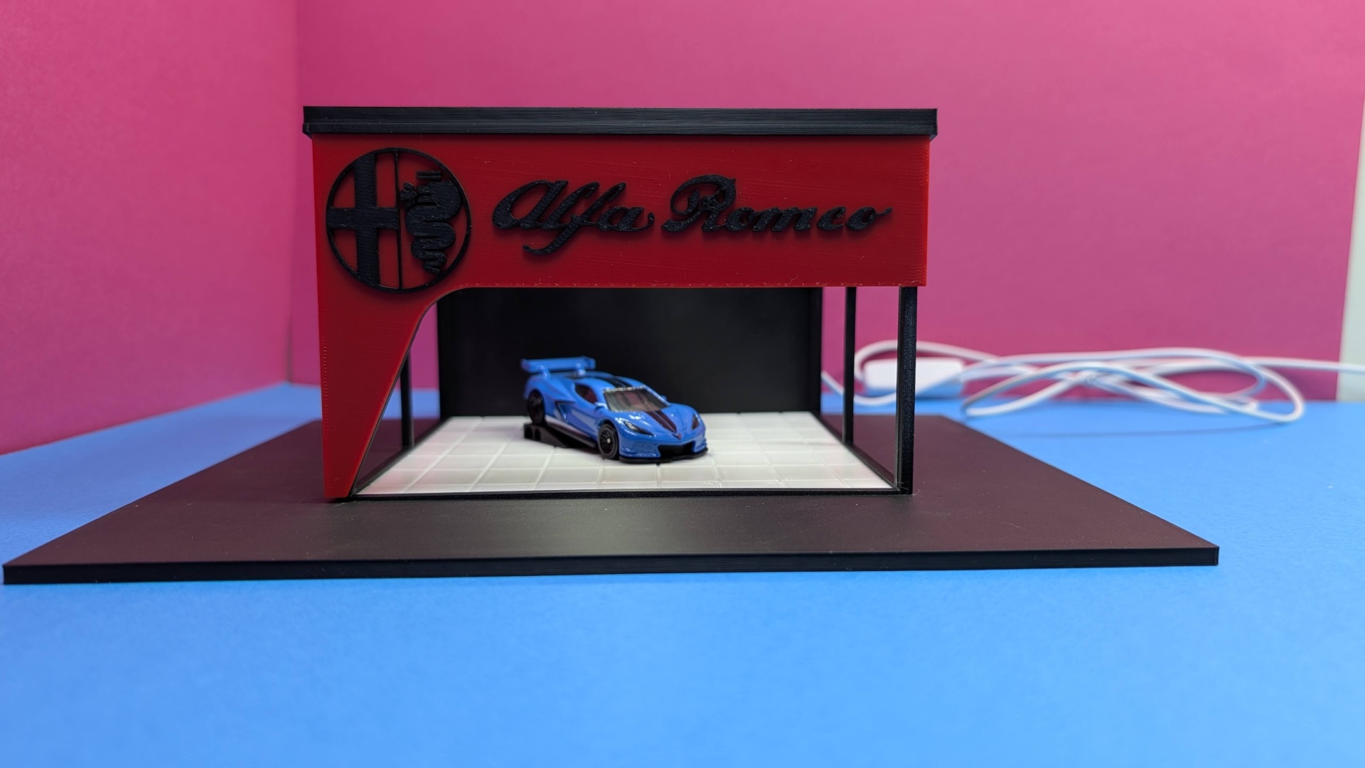 Miniatura de carro desportivo azul em exposição com fachada Alfa Romeo vermelha e cenário preto e branco