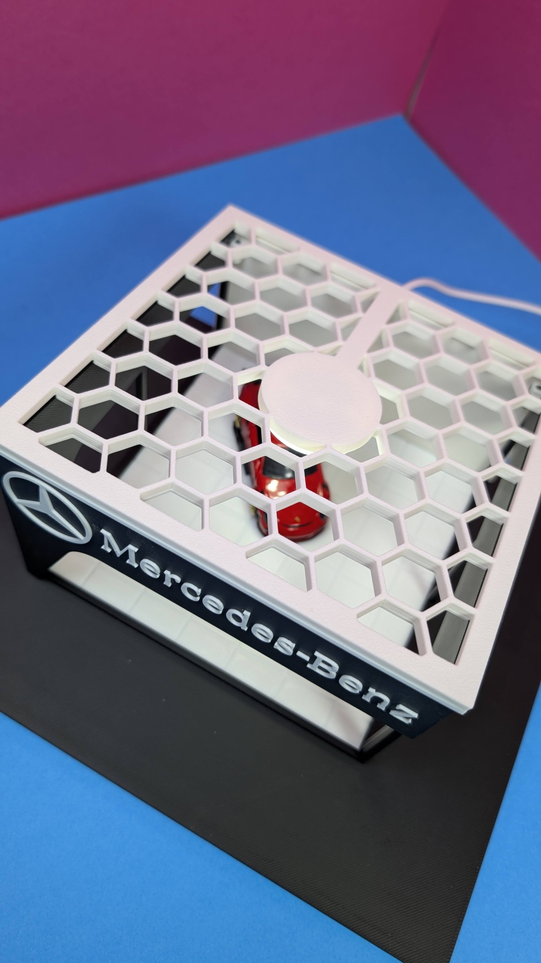 Miniatura de carro vermelho dentro de caixa com grelha hexagonal e logótipo Mercedes-Benz