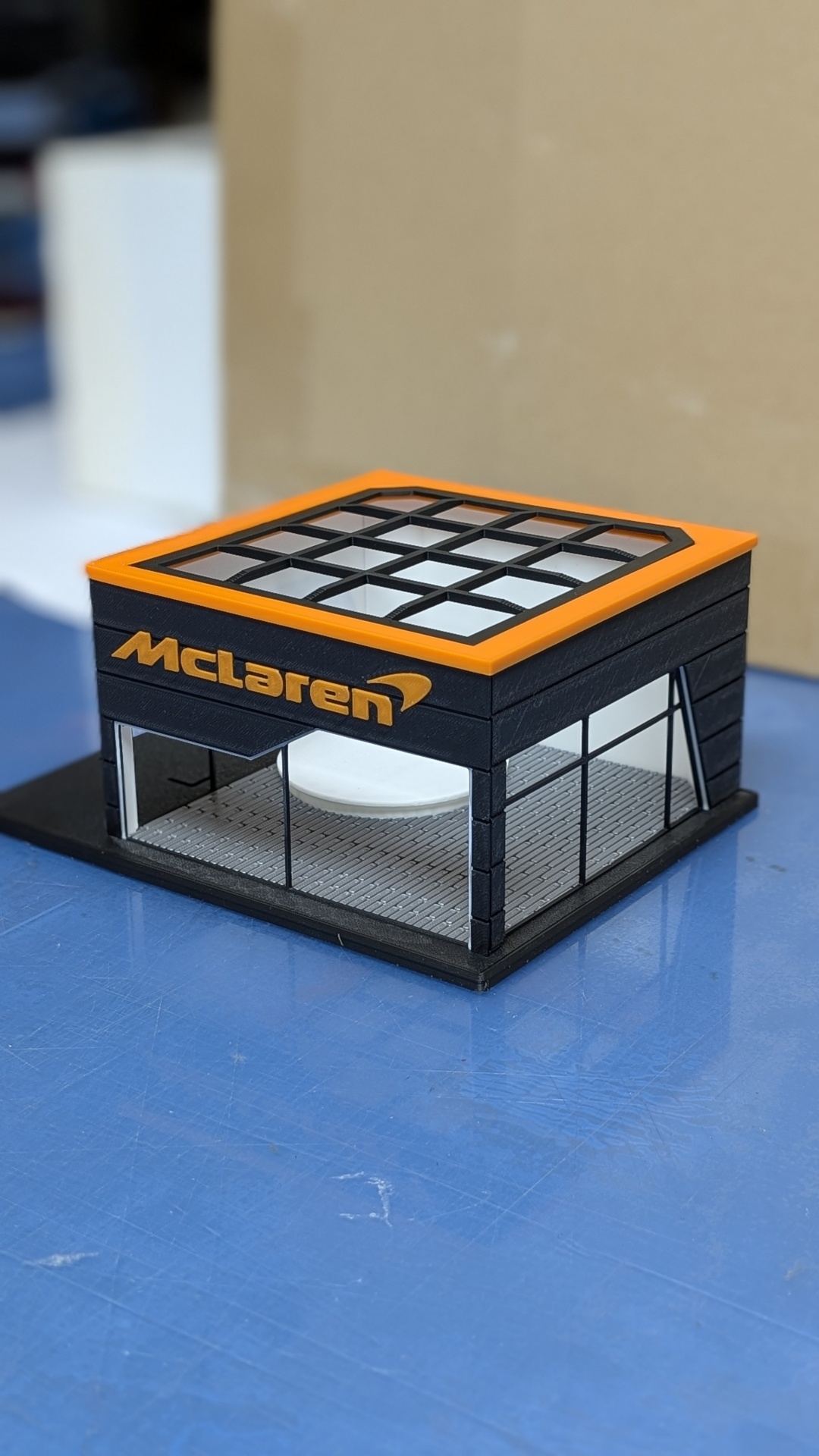 Miniatura de prédio com estrutura preta, topo laranja e marca McLaren