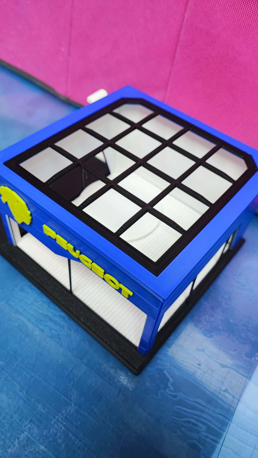 Miniatura de estrutura arquitetónica azul com janelas transparentes e texto PEUGEOT amarelo