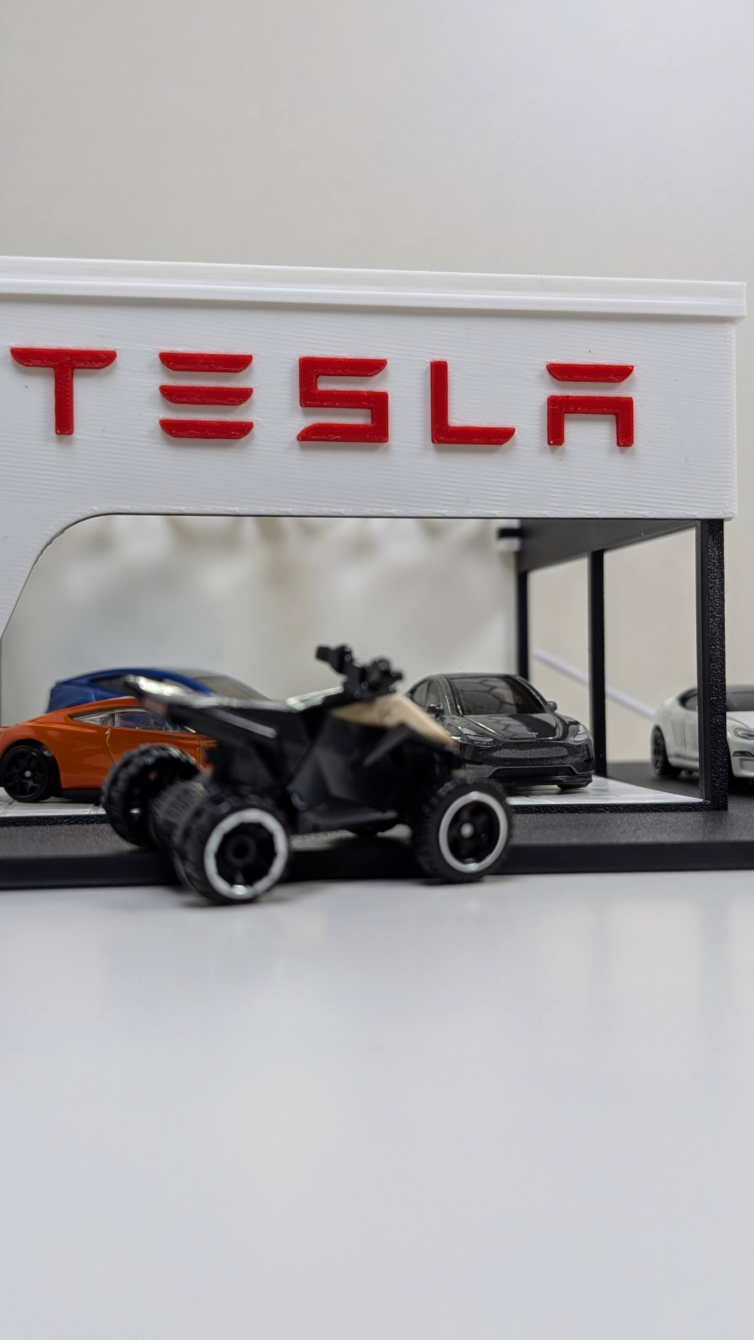 Miniatura de loja Tesla com carros e veículo todo-o-terreno preto em primeiro plano.