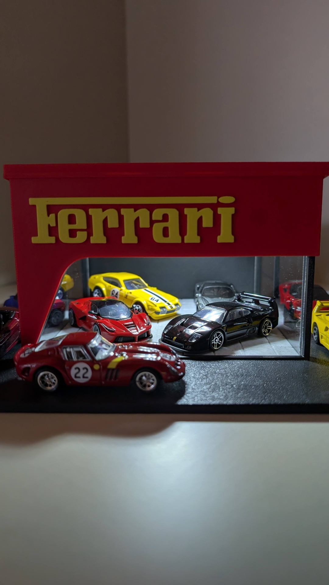 Carros miniatura Ferrari de várias cores dentro de expositor vermelho com texto amarelo Ferrari