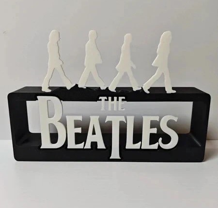 Escultura das letras THE BEATLES e figuras dos membros da banda numa base preta.
