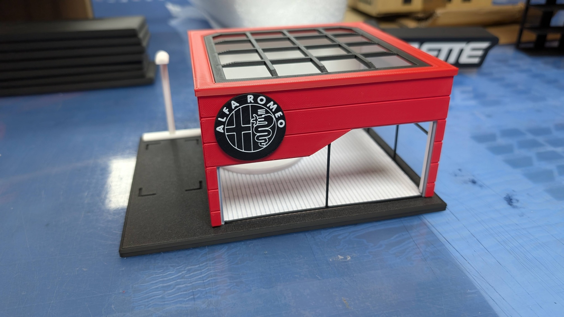 Miniatura de prédio vermelho com janelas de vidro e logo ALFA ROMEO em fundo azul