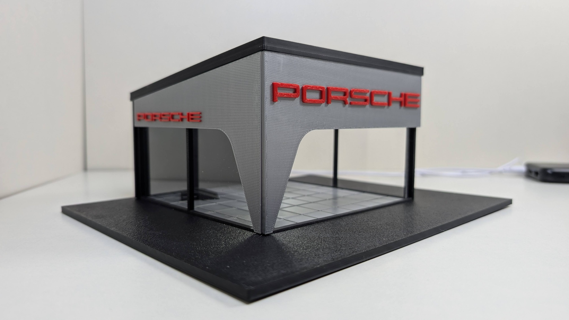 Miniatura de fachada de edifício cinzento com letras vermelhas Porsche e base preta.