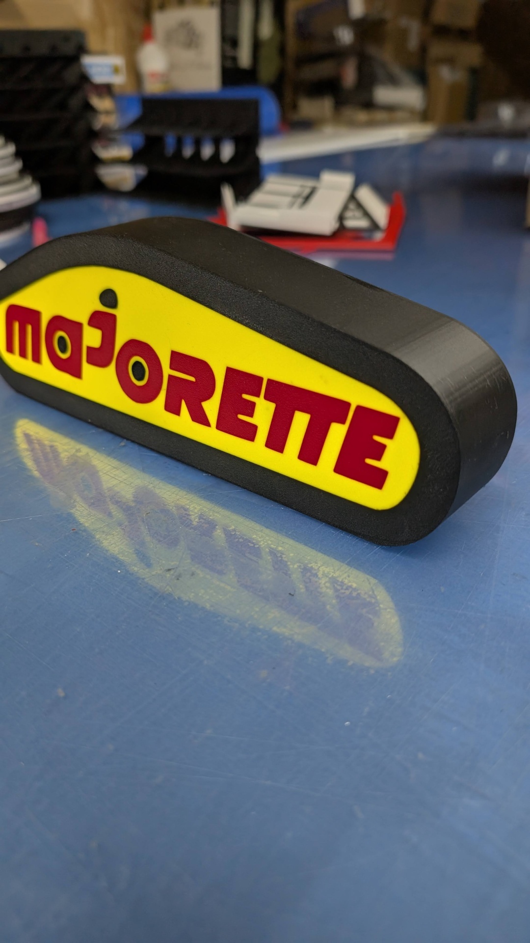 Objeto de plástico preto com face amarela e texto vermelho majorette sobre superfície azul