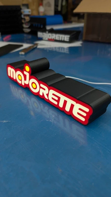 Objeto preto com palavra majorette em letras vermelhas e brancas sobre superfície azul