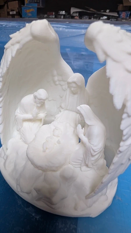 Escultura branca de Natividade com figuras e anjo com asas abertas