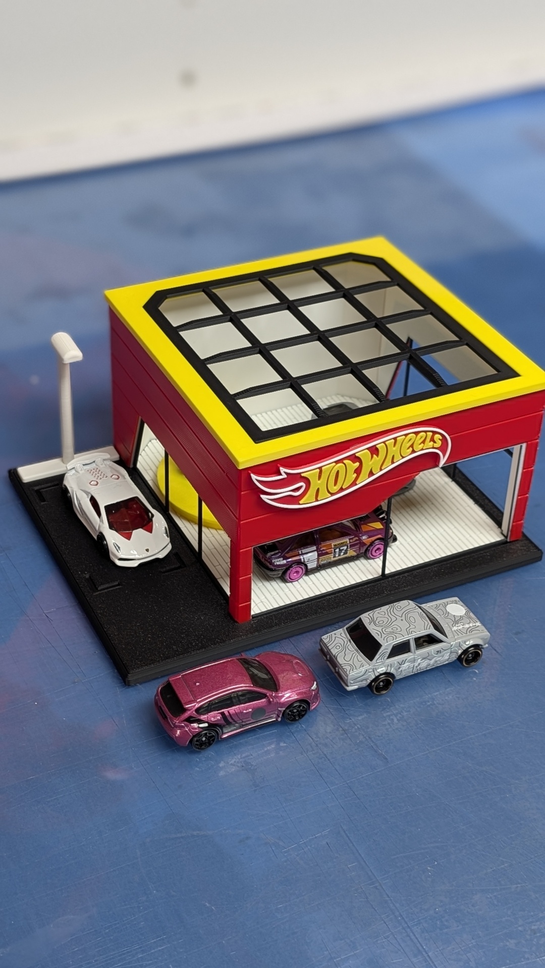 Garagem Hot Wheels de plástico com quatro carrinhos de brinquedo de diferentes cores em superfície azul.