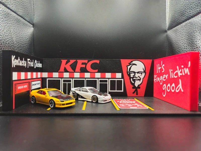 Miniaturas de carros num parque de estacionamento miniatura com fachada da KFC e texto promocional