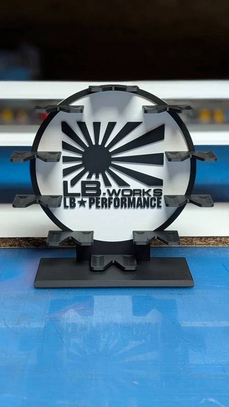 Suporte de plástico preto com texto LB WORKS LB PERFORMANCE e logotipo de sol