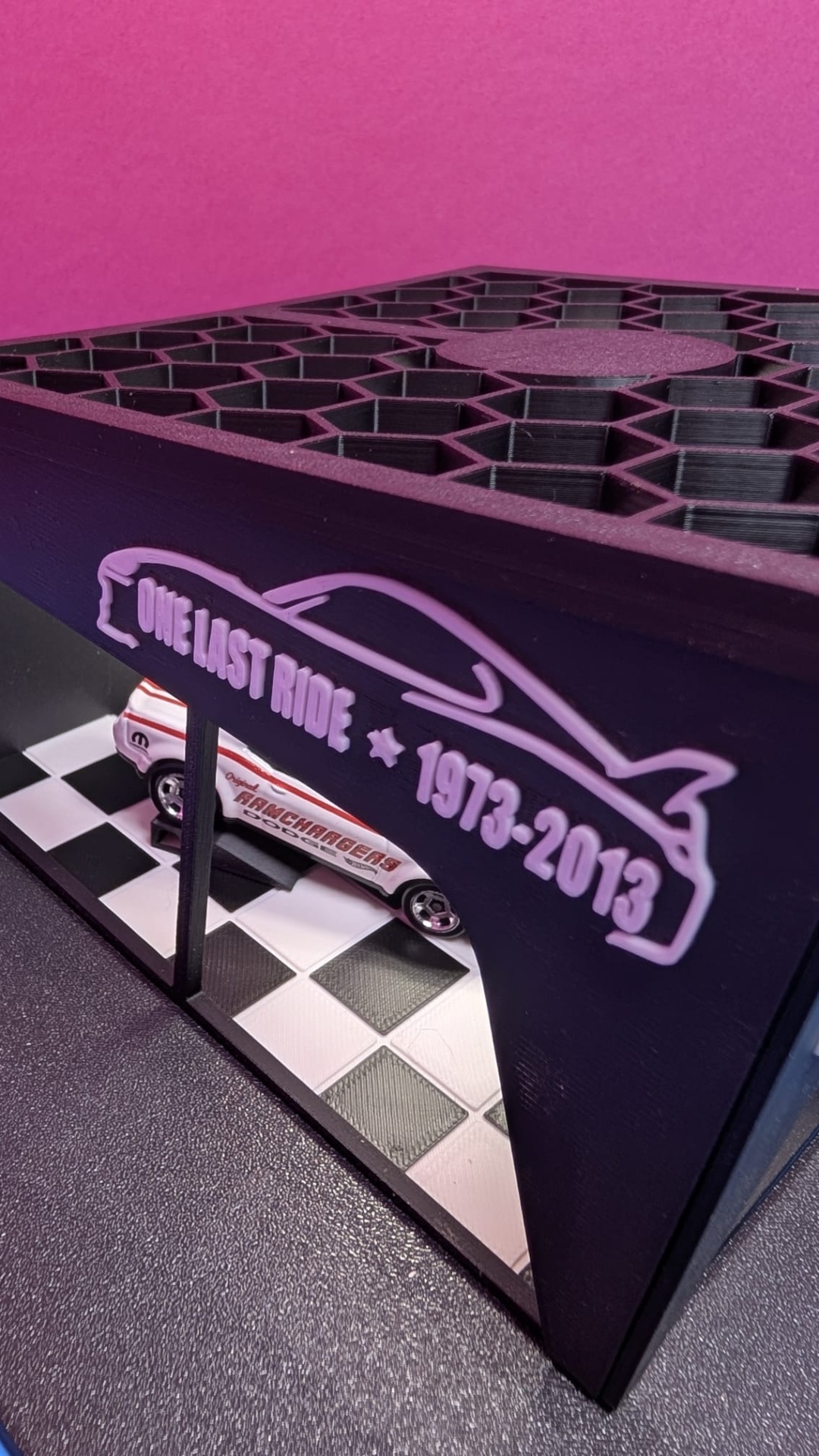 Miniatura de carro branco com detalhes vermelhos numa base com padrão xadrez preto e branco e estrutura com texto lilás