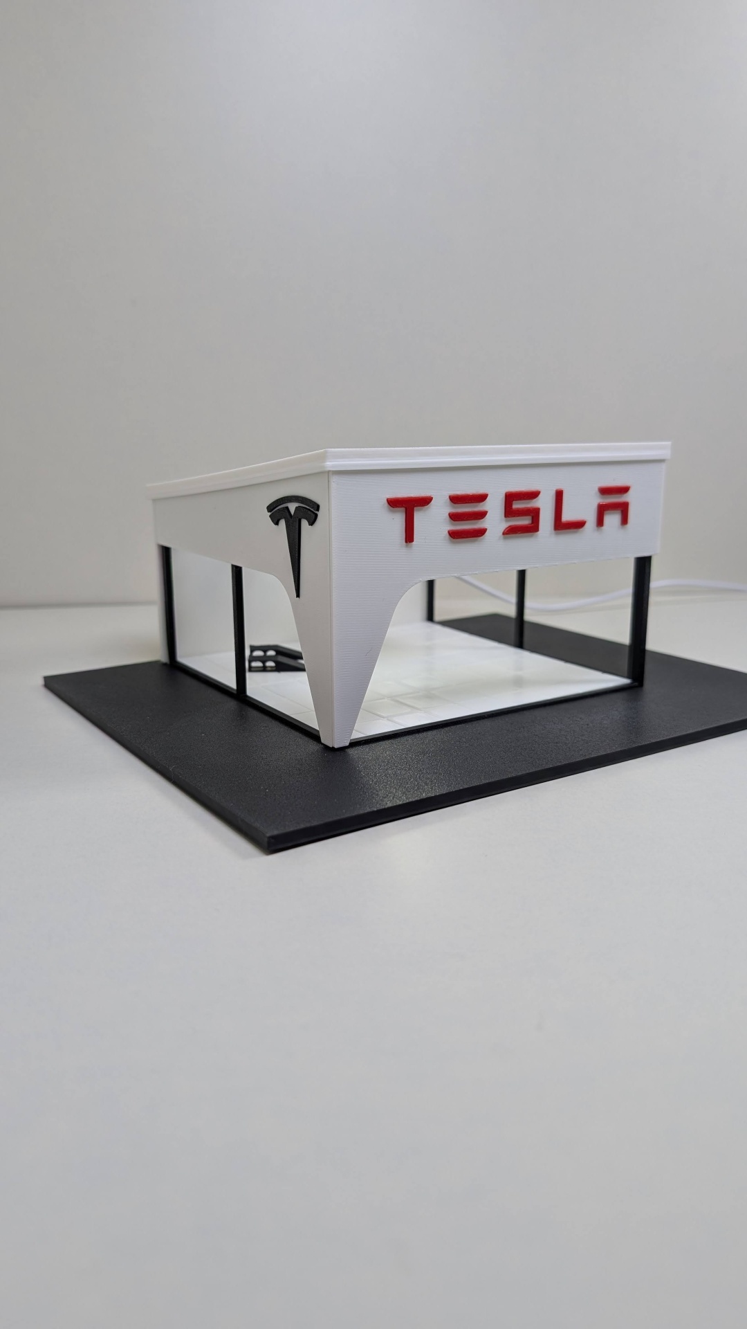 Maqueta da loja Tesla sobre base preta com logotipos em vermelho e preto
