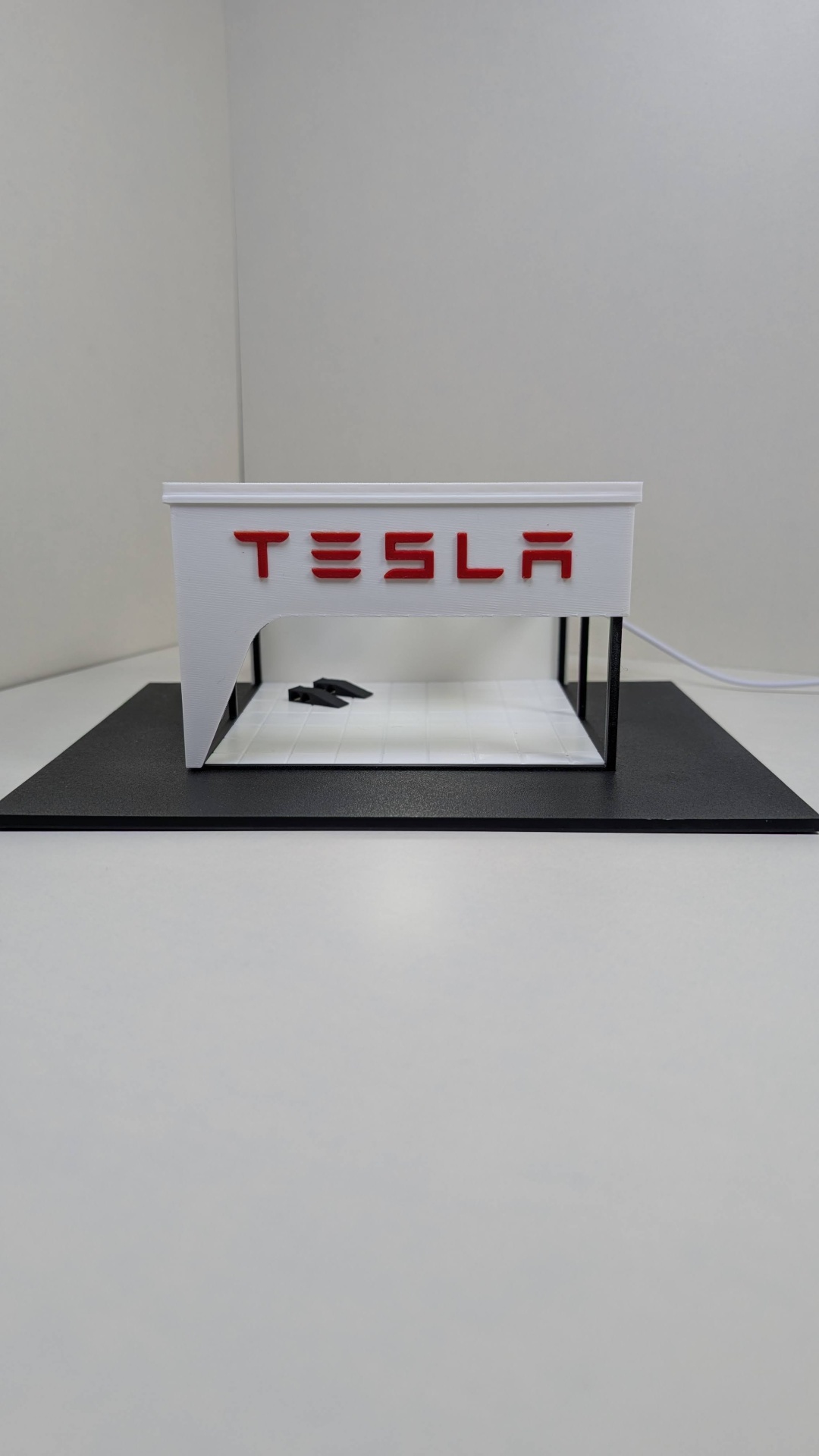 Miniatura de estrutura branca com logótipo TESLA em vermelho e suporte preto