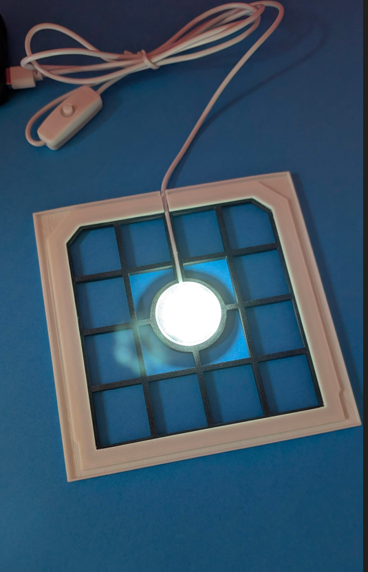 Aparelho quadrado branco com grelha preta e luz circular acesa no centro