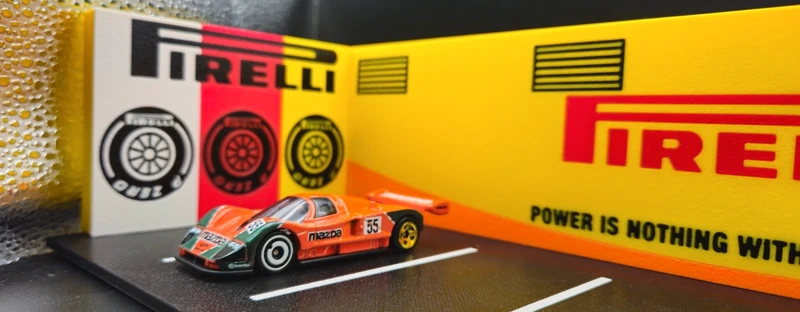 Miniatura de carro de corrida Mazda laranja número 55 com fundo PIRELLI e estrada