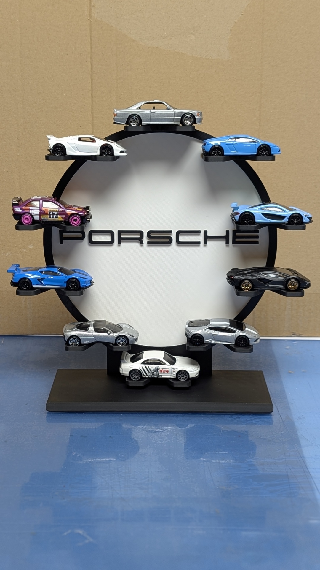 Miniaturas de carros desportivos coloridos numa exposição com círculo branco e texto PORSCHE