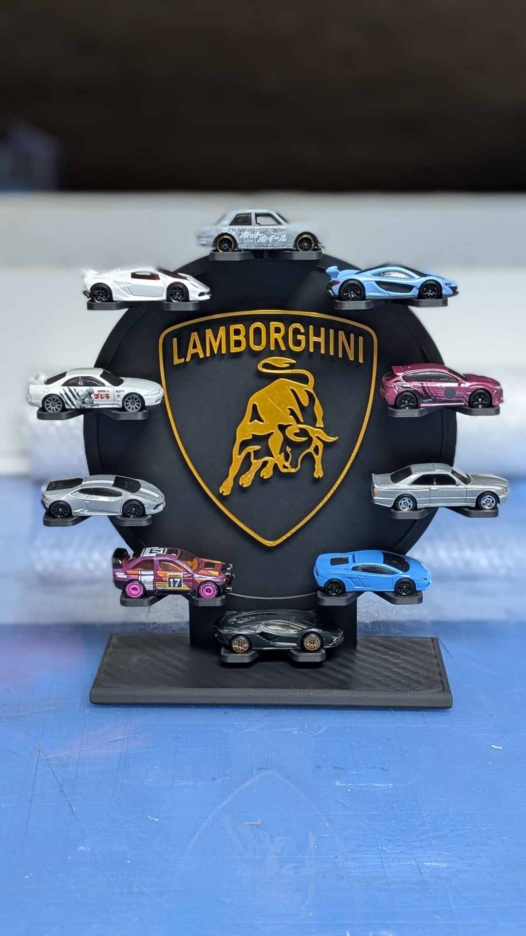Doze carrinhos de brinquedo em miniatura numa base preta com logo Lamborghini