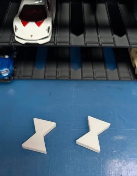 Dois mini carros de brinquedo numa estante preta com duas peças brancas triangulares em cima de superfície azul