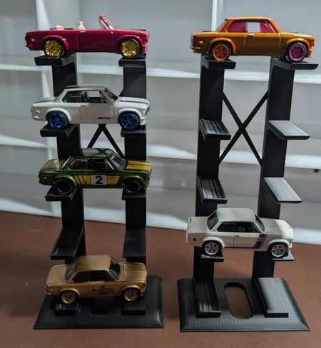 Cinco carros de brinquedo coloridos expostos em suportes pretos sobre superfície castanha