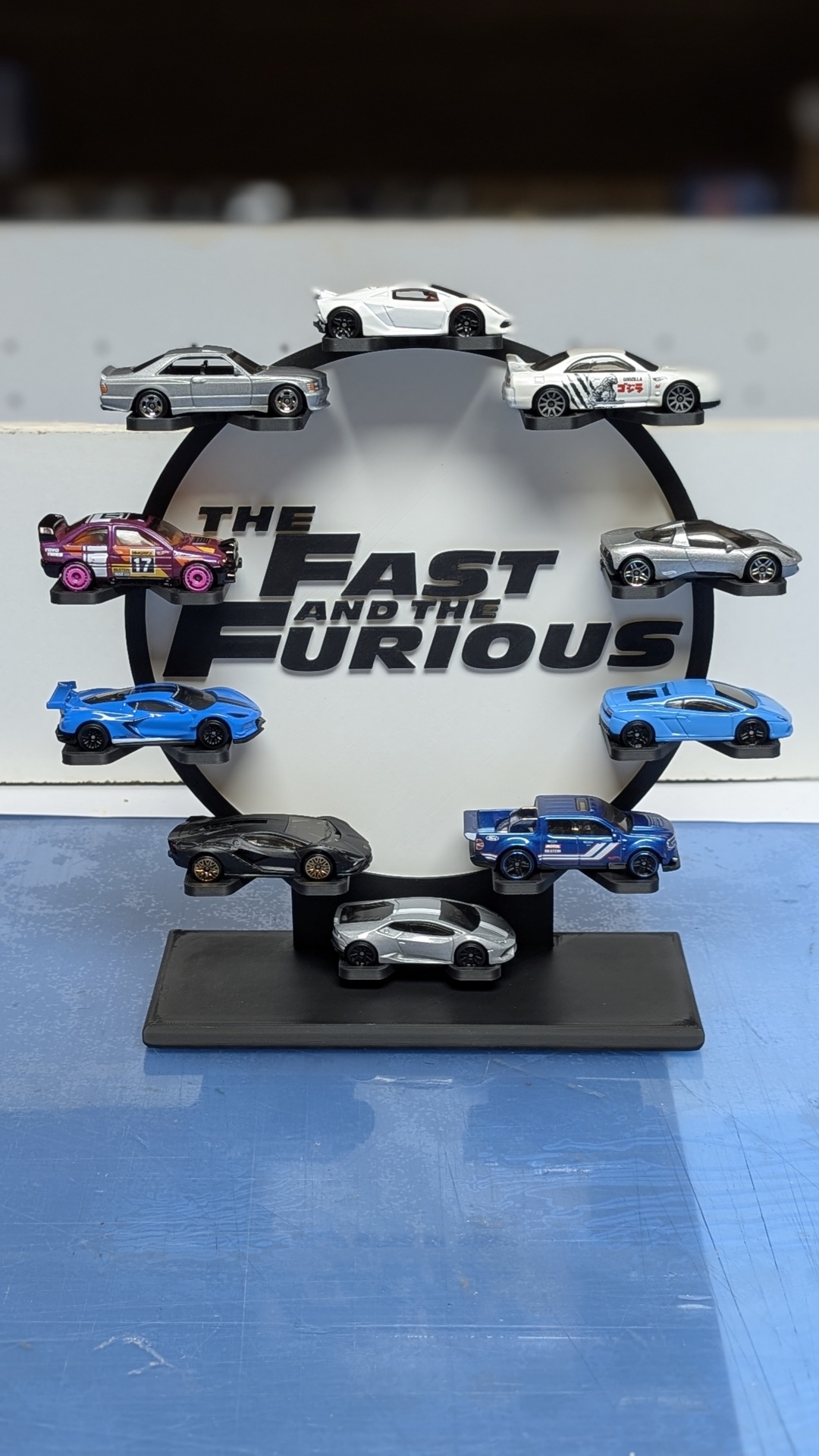 Miniaturas de carros desportivos em suporte circular com o texto THE FAST AND THE FURIOUS ao fundo