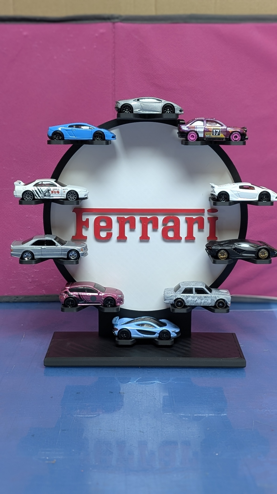 Exposição circular com carros de brinquedo coloridos em torno do texto Ferrari