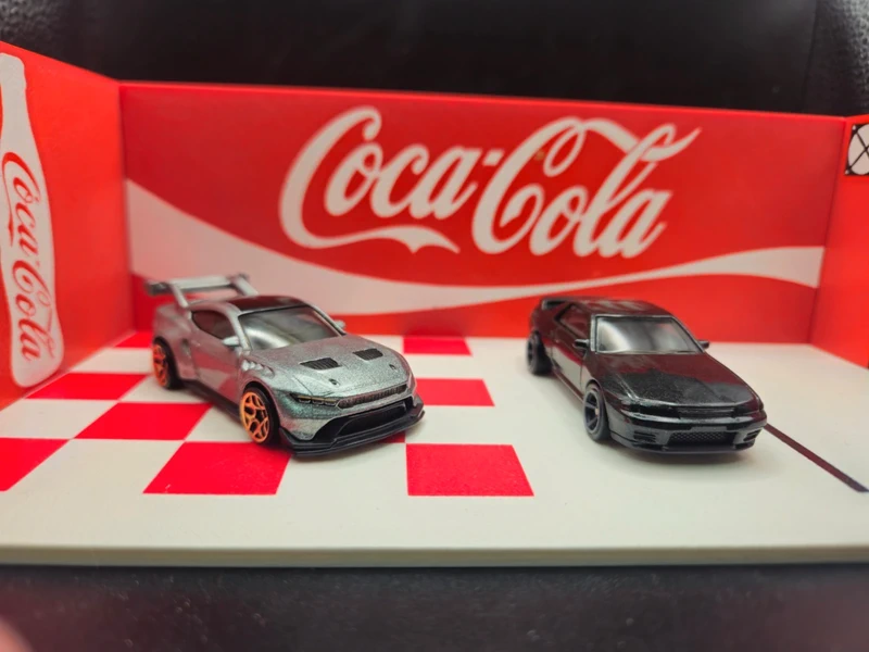 Miniaturas de carros cinza e preto com base branca de padrão xadrez vermelho e fundo vermelho com logo Coca-Cola
