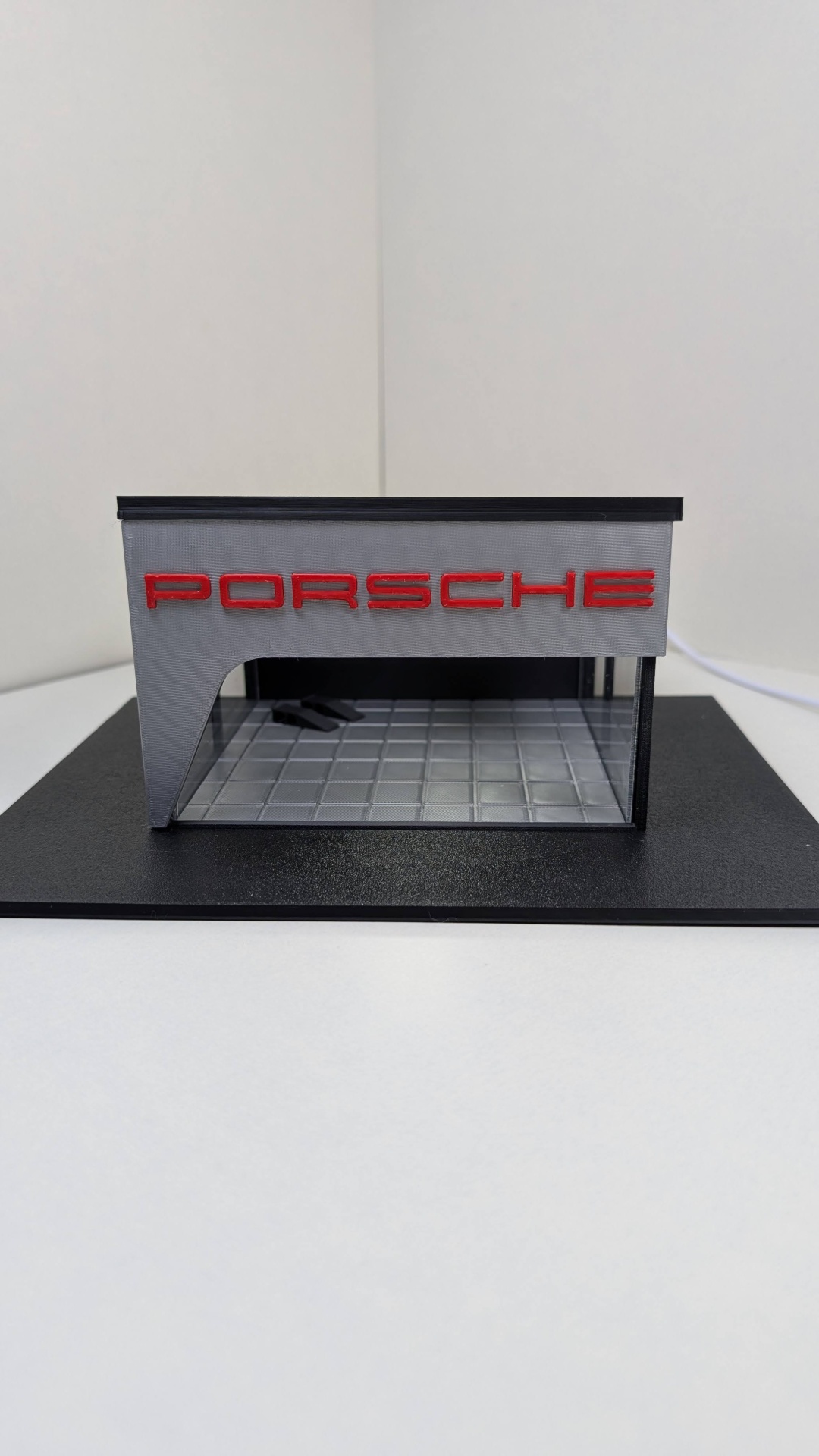 Miniatura de garagem com placa PORSCHE e chão quadriculado