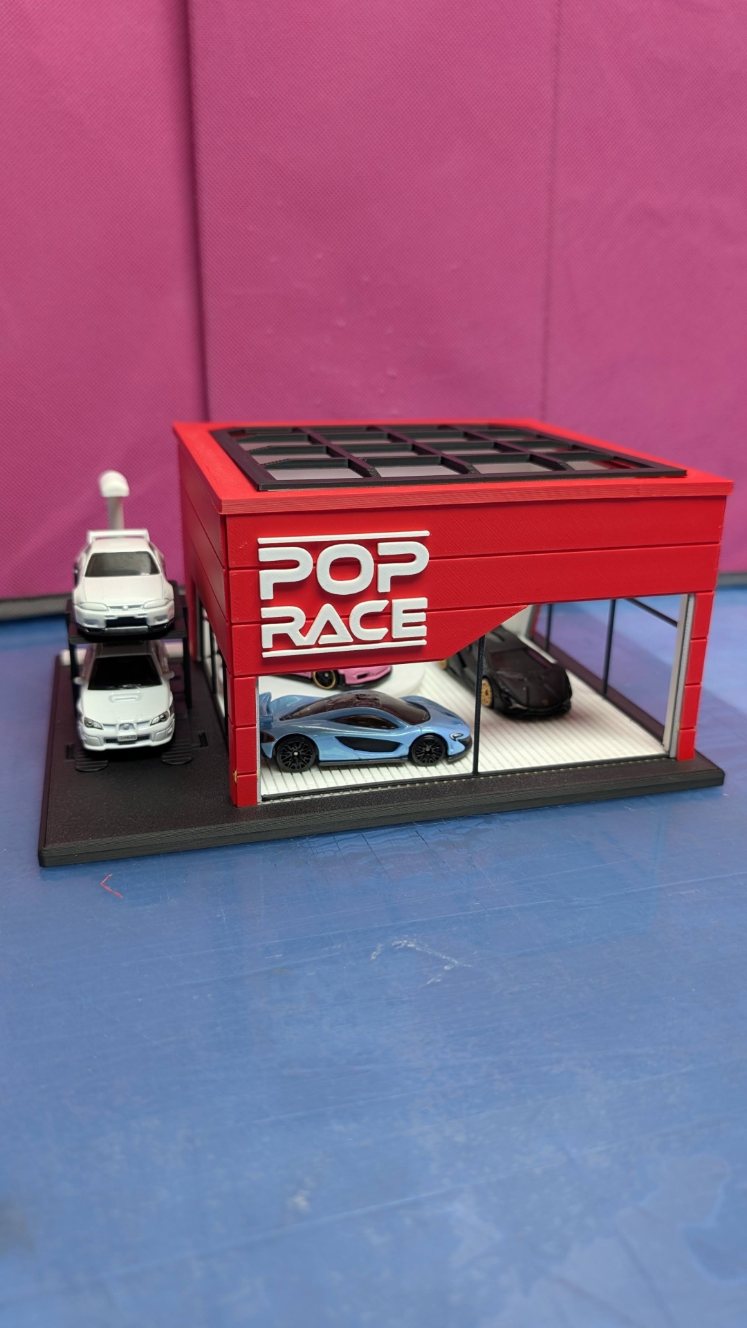 Maqueta de garagem vermelha com carros em miniatura e texto POP RACE