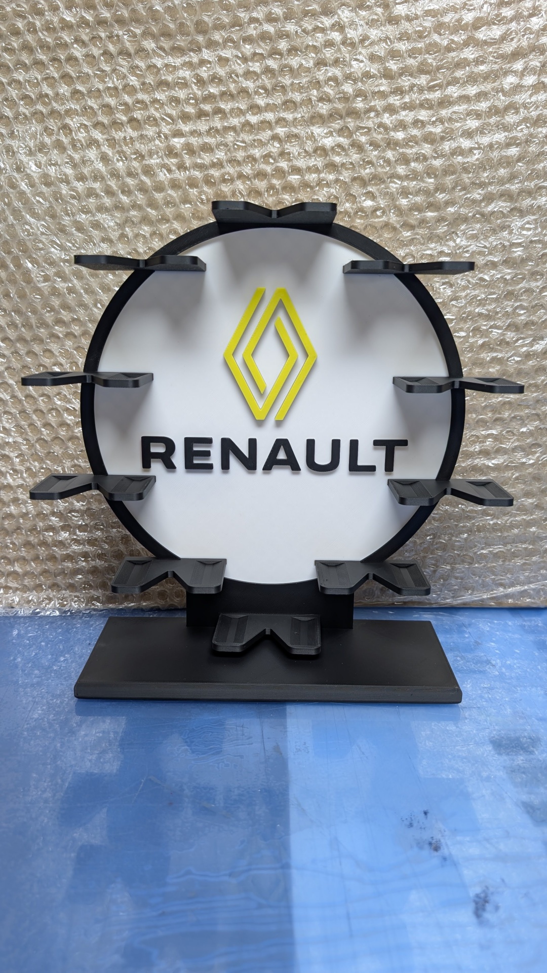 Expositor plástico preto e branco com logotipo Renault amarelo e preto em fundo branco e suportes para pendurar.