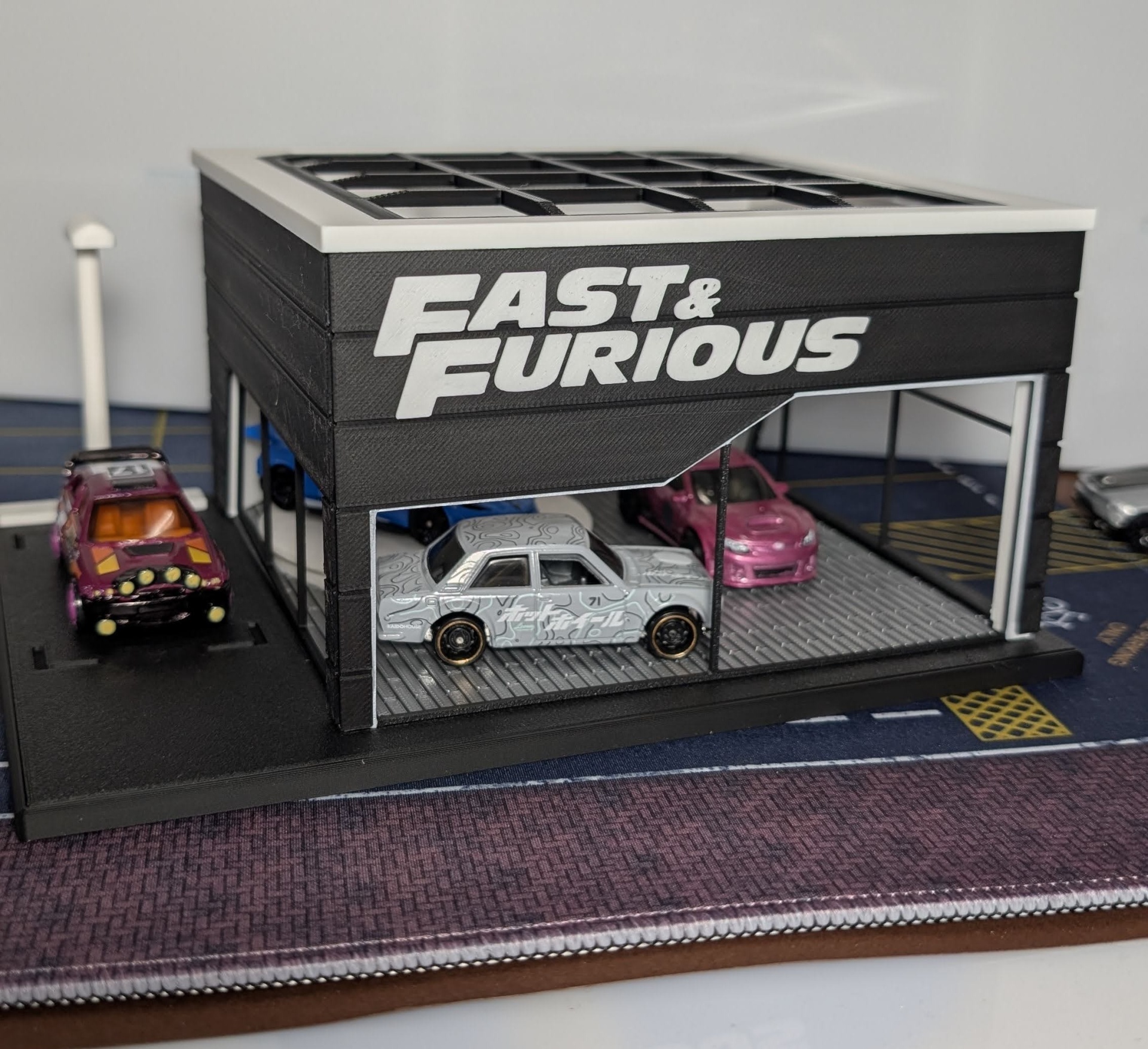 Garagem em miniatura preta com texto FAST & FURIOUS e carros em miniatura