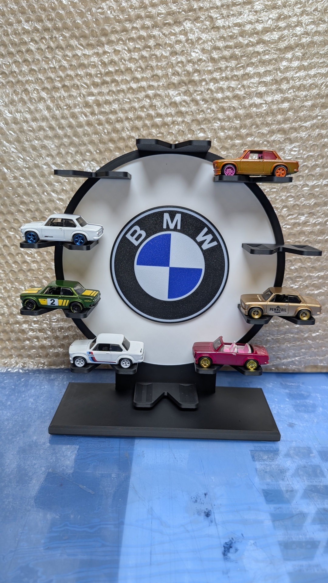 Suporte preto para carros miniatura com logótipo BMW ao centro e seis carros de coleção coloridos expostos