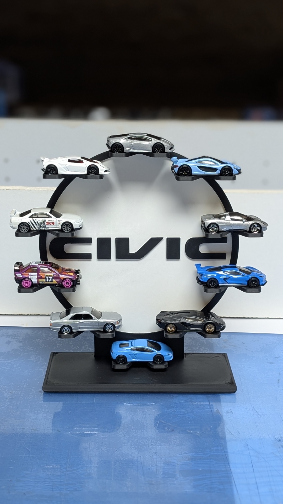 Expositor circular preto com carros em miniatura e texto CIVIC ao fundo.