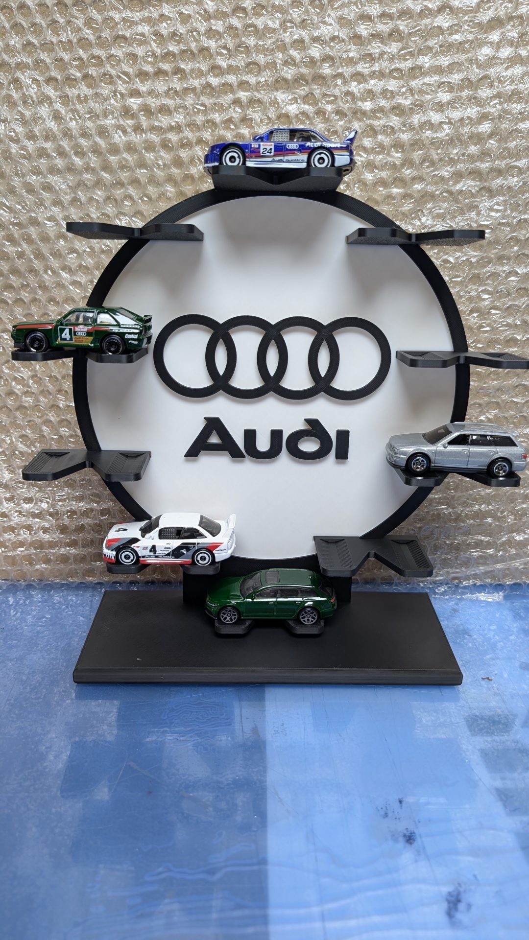 Expositor circular preto com miniaturas de carros e logótipo Audi em fundo branco