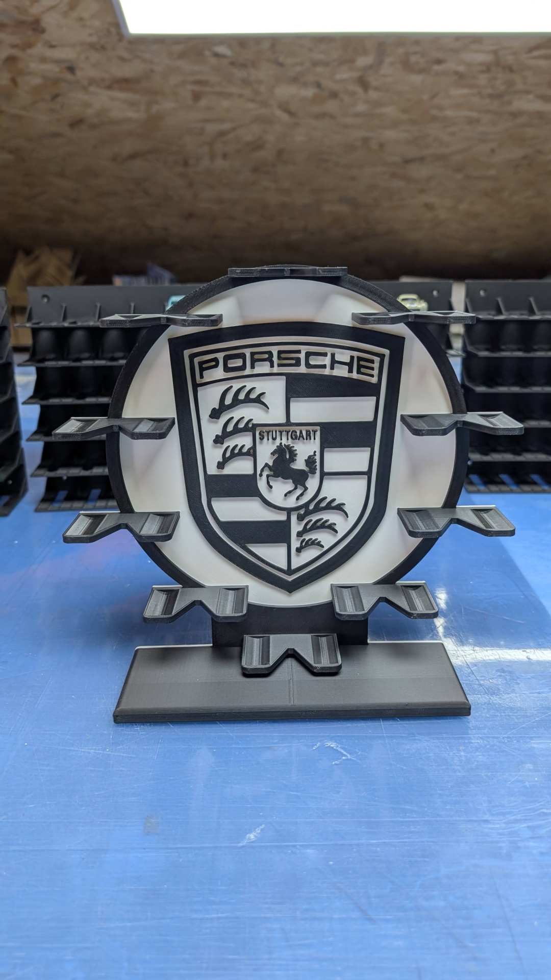 Emblema Porsche preto e branco em plástico numa superfície azul.