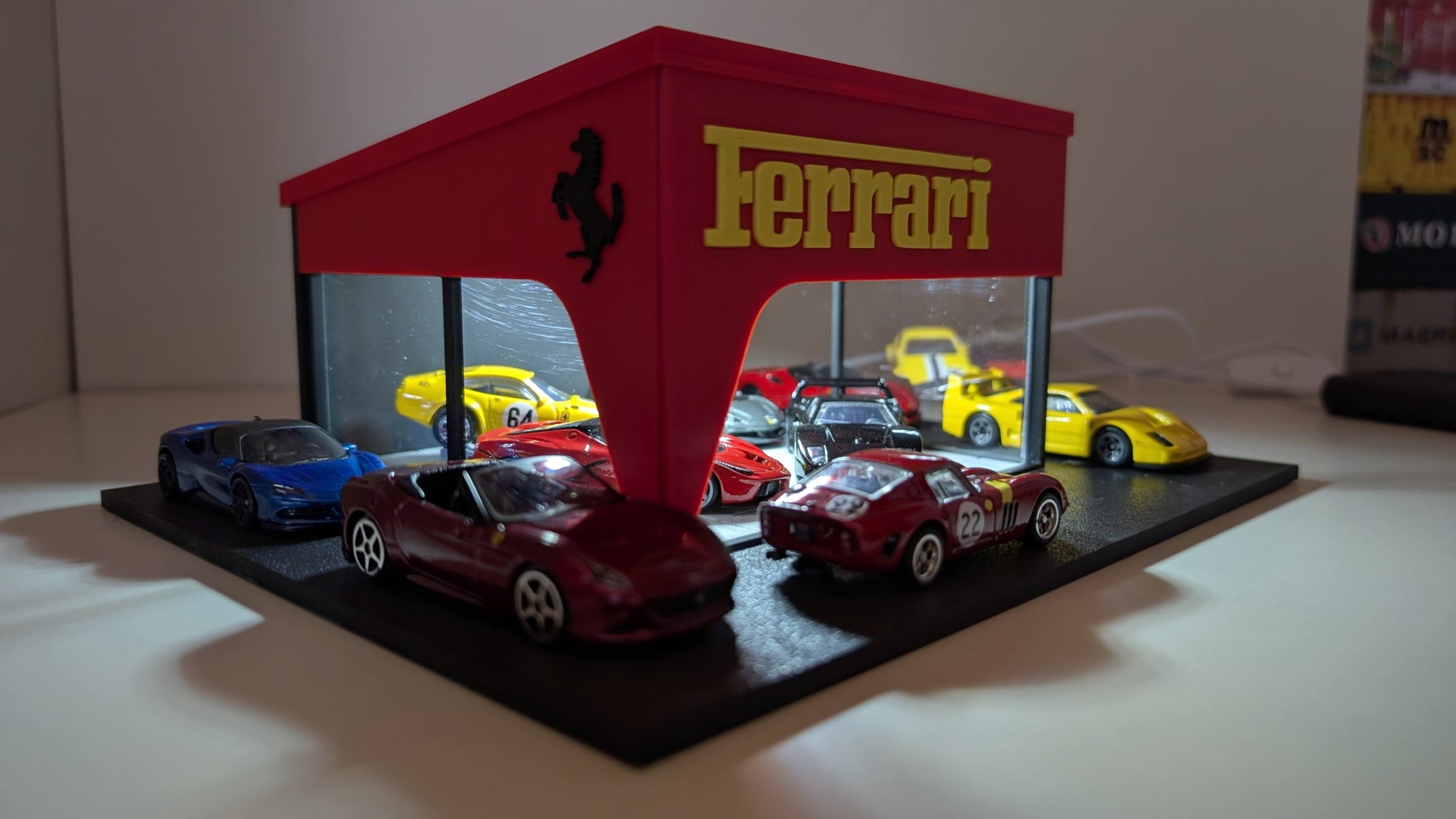 Miniaturas de carros Ferrari em exposição numa estrutura vermelha com logo Ferrari.