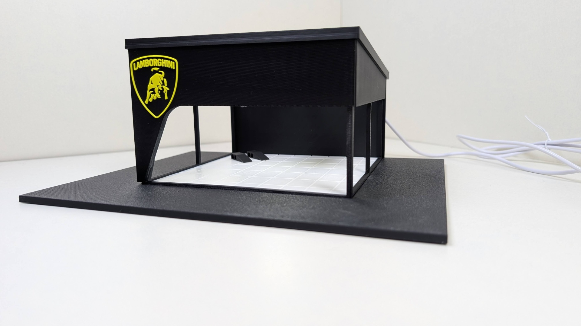 Maqueta de garagem preta com chão branco em padrão de azulejo e logótipo Lamborghini amarelo.