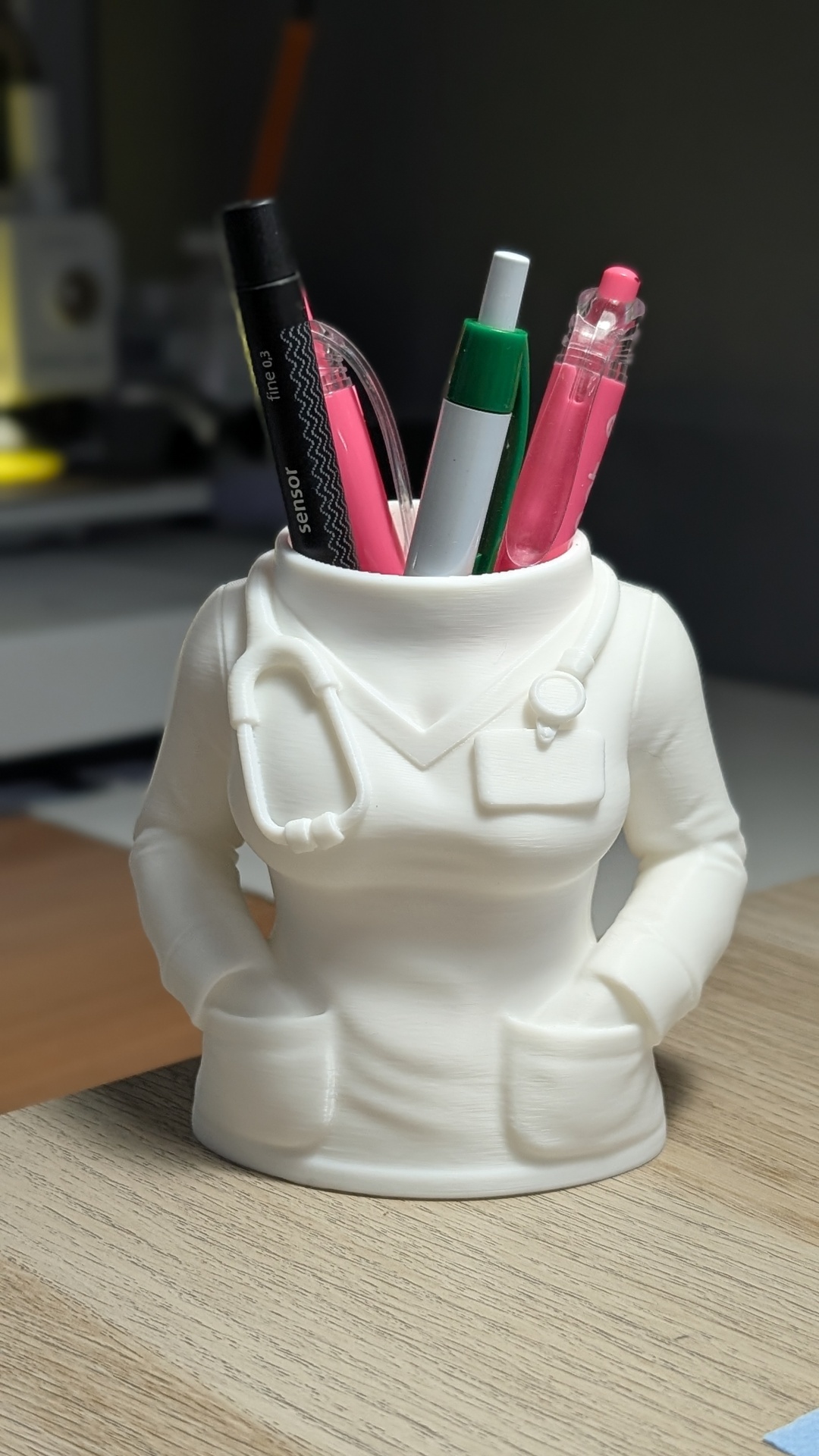 Suporte de canetas branco em formato de uniforme médico com canetas de várias cores.