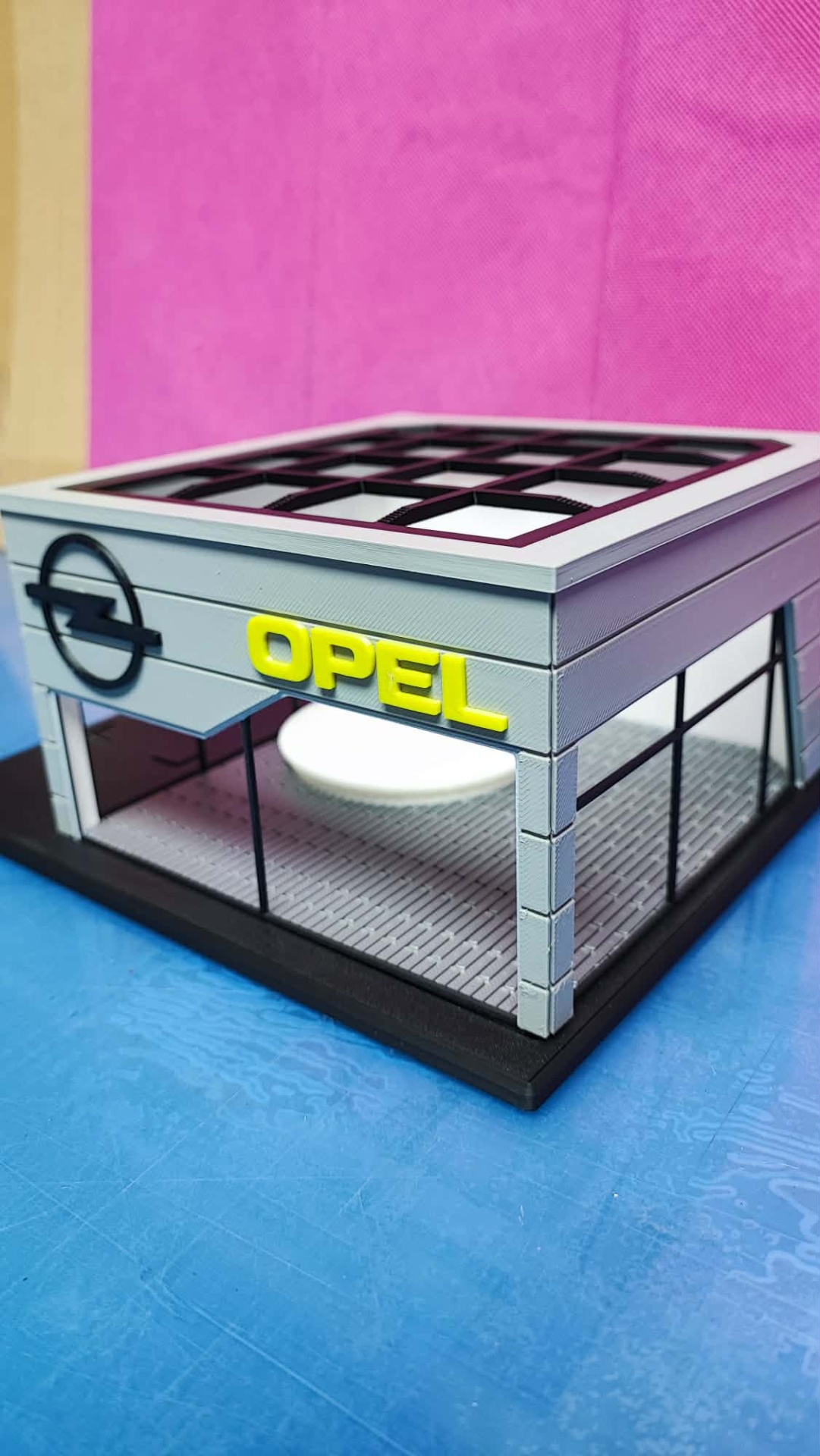 Miniatura de uma garagem Opel cinzenta com letras amarelas e janelas de vidro