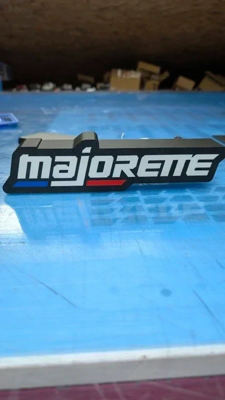 Emblema preto com texto majorette branco e linhas azul e vermelha sobre superfície azul