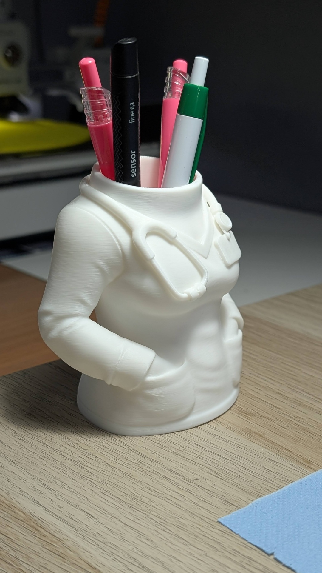 Porta-canetas branco formato torso de médico com canetas coloridas sobre mesa clara