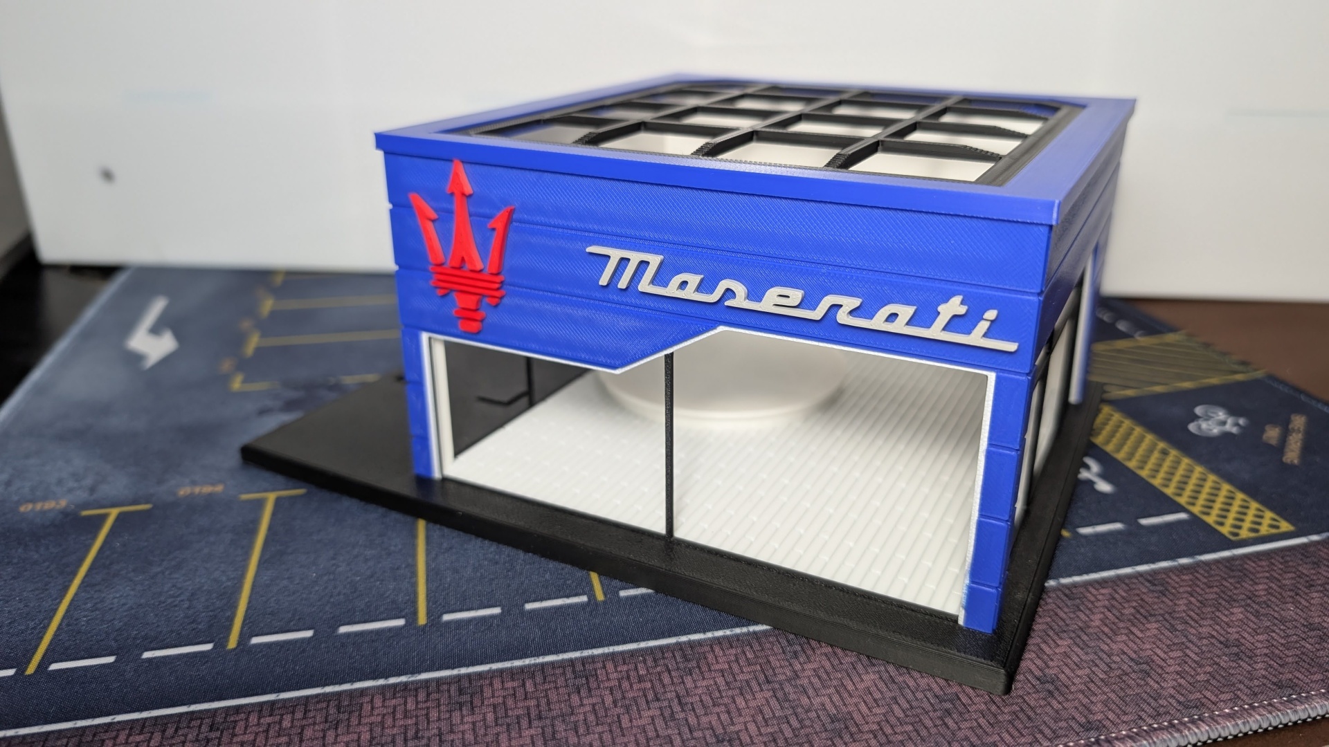Miniatura de estrutura azul com logo e texto Maserati em relevo prateado e símbolo vermelho.
