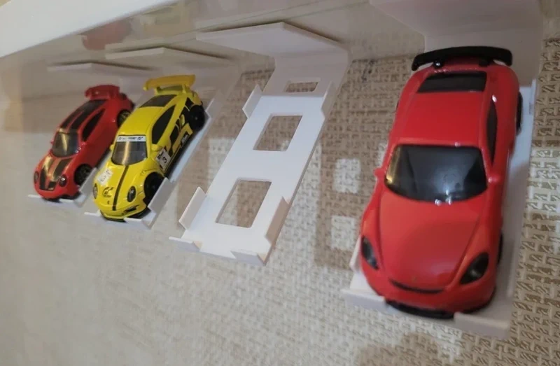 Três carrinhos de brinquedo coloridos em suporte branco numa superfície clara