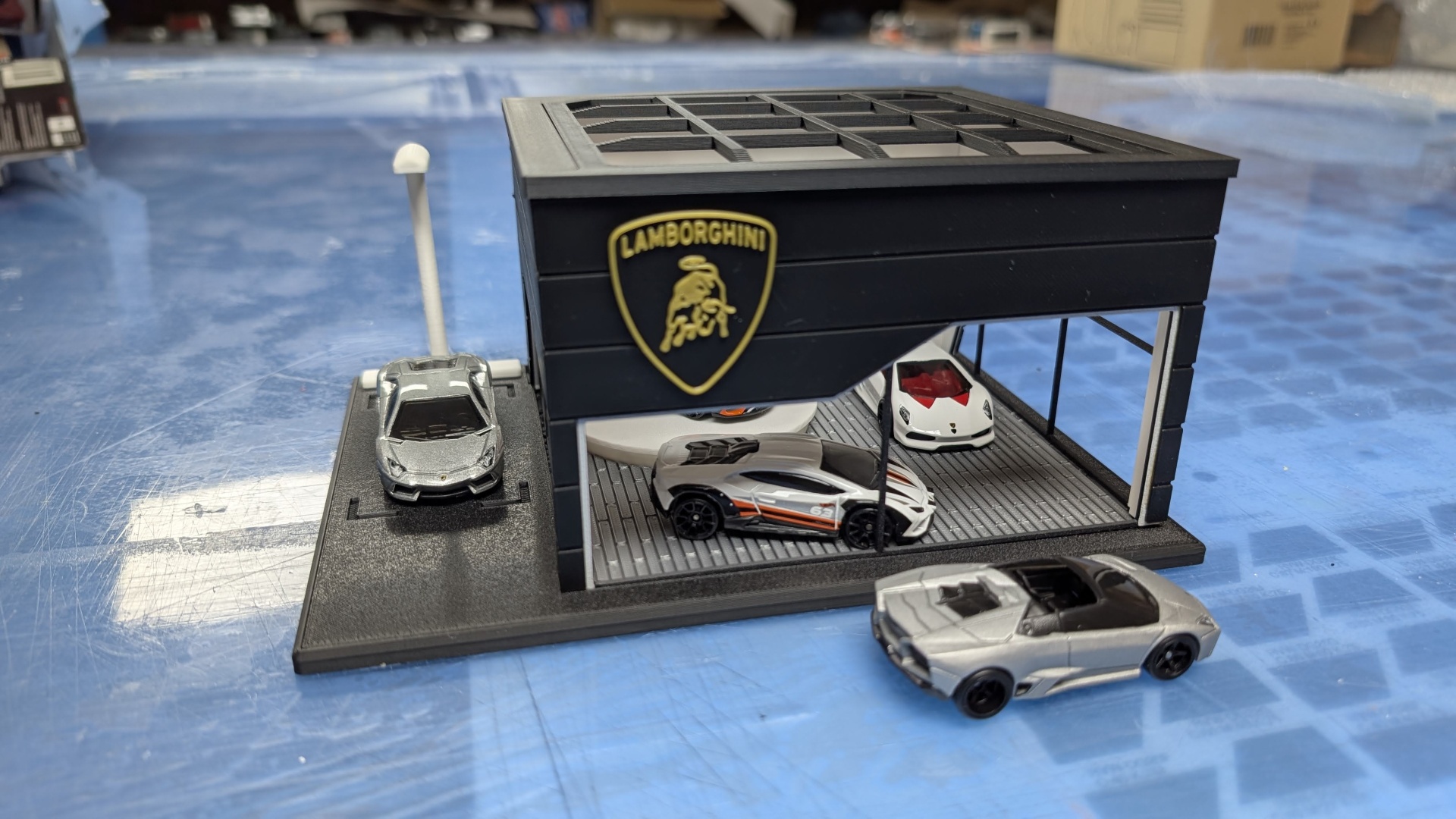Miniatura garagem Lamborghini preta com quatro carros desportivos em miniatura.