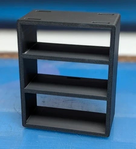 Estante pequena preta de plástico com três prateleiras em mesa azul