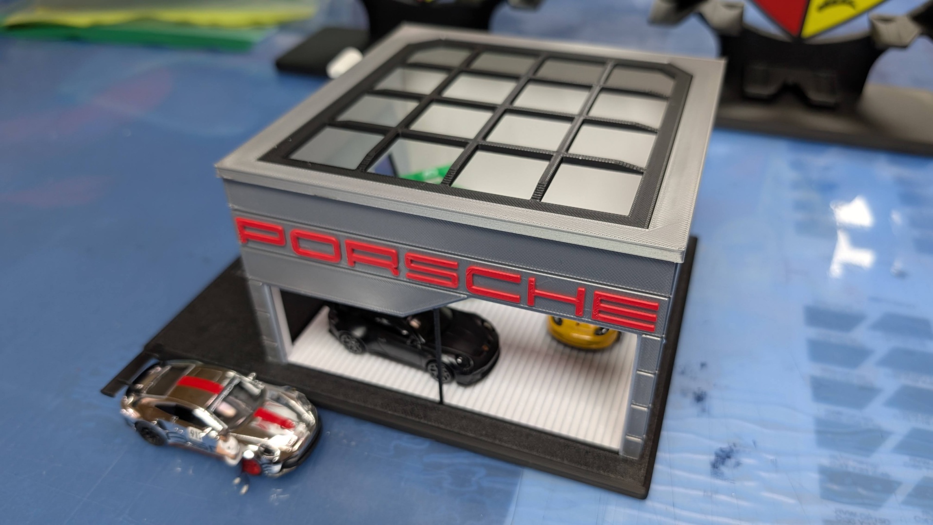 Miniatura de loja Porsche com carros miniatura dentro e fora, em plástico cinzento, preto e vidro